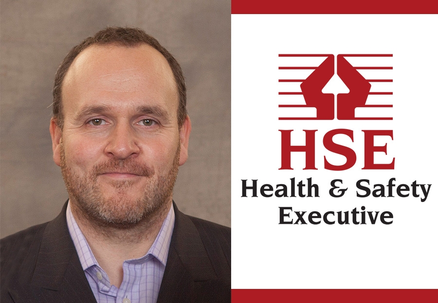 A man in a suit is smiling slightly, pictured next to the red and white logo of the Health & Safety Executive (HSE) featuring a stylized arrow and text.