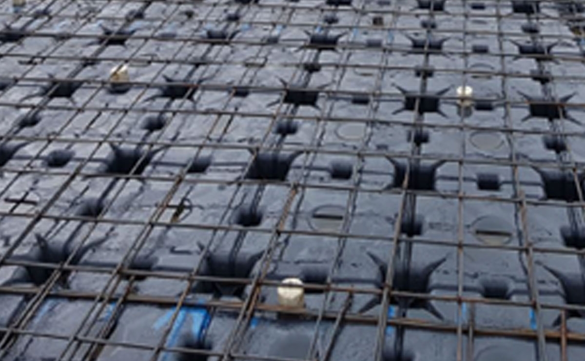 Close-up view of a construction site showing a grid of steel reinforcement bars (rebar) placed over modular plastic void formers, used as part of a concrete slab system.