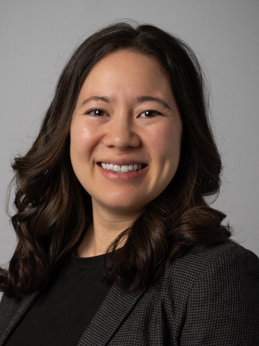 Professional woman smiling, dark wavy hair, gray patterned blazer.