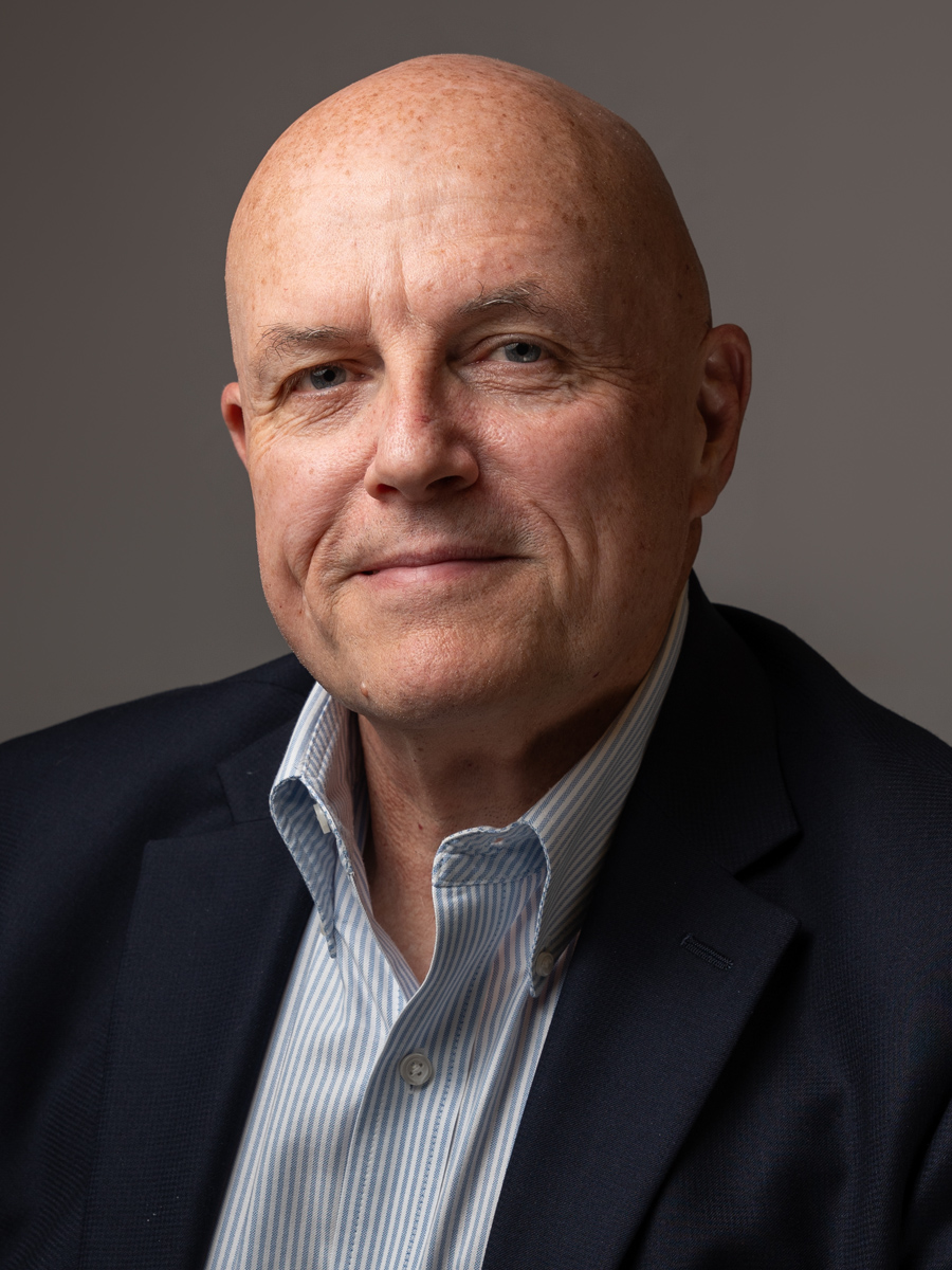 A man looks confidently at the camera. He is wearing a dark blazer over a light blue dress shirt.