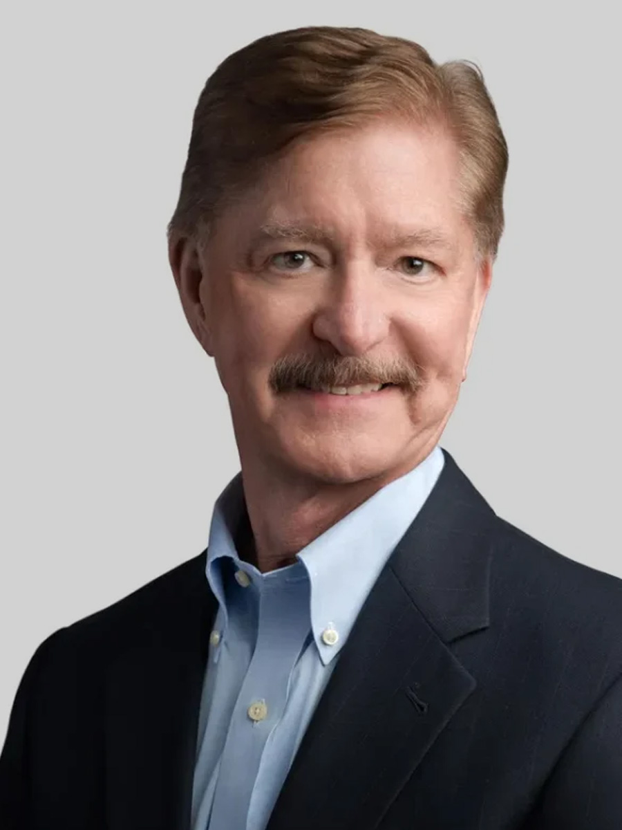A man smiles into the camera for a headshot. He is wearing a dark blazer over a light blue dress shirt.