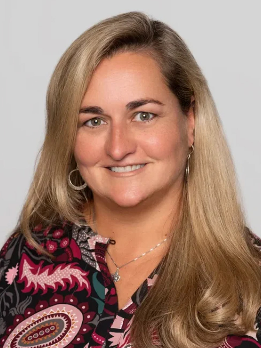 A woman wearing a bright colored patterned blouse smiles for the camera in a professional headshot.
